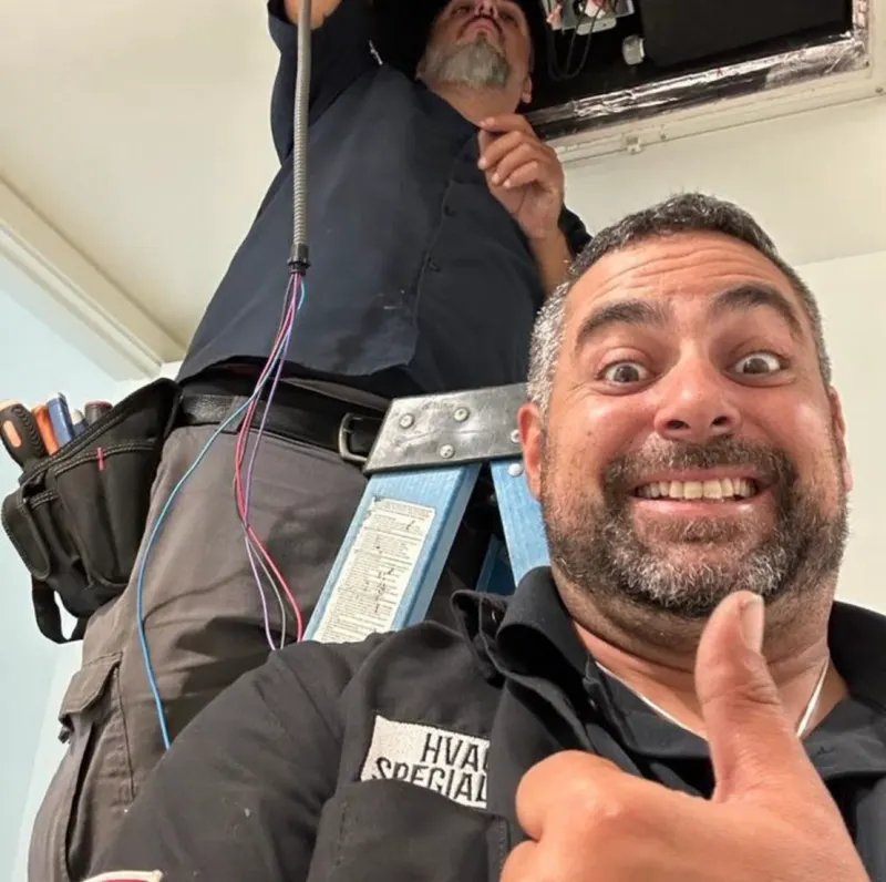 Two Boost technicians at work, one on a ladder at a ceiling opening