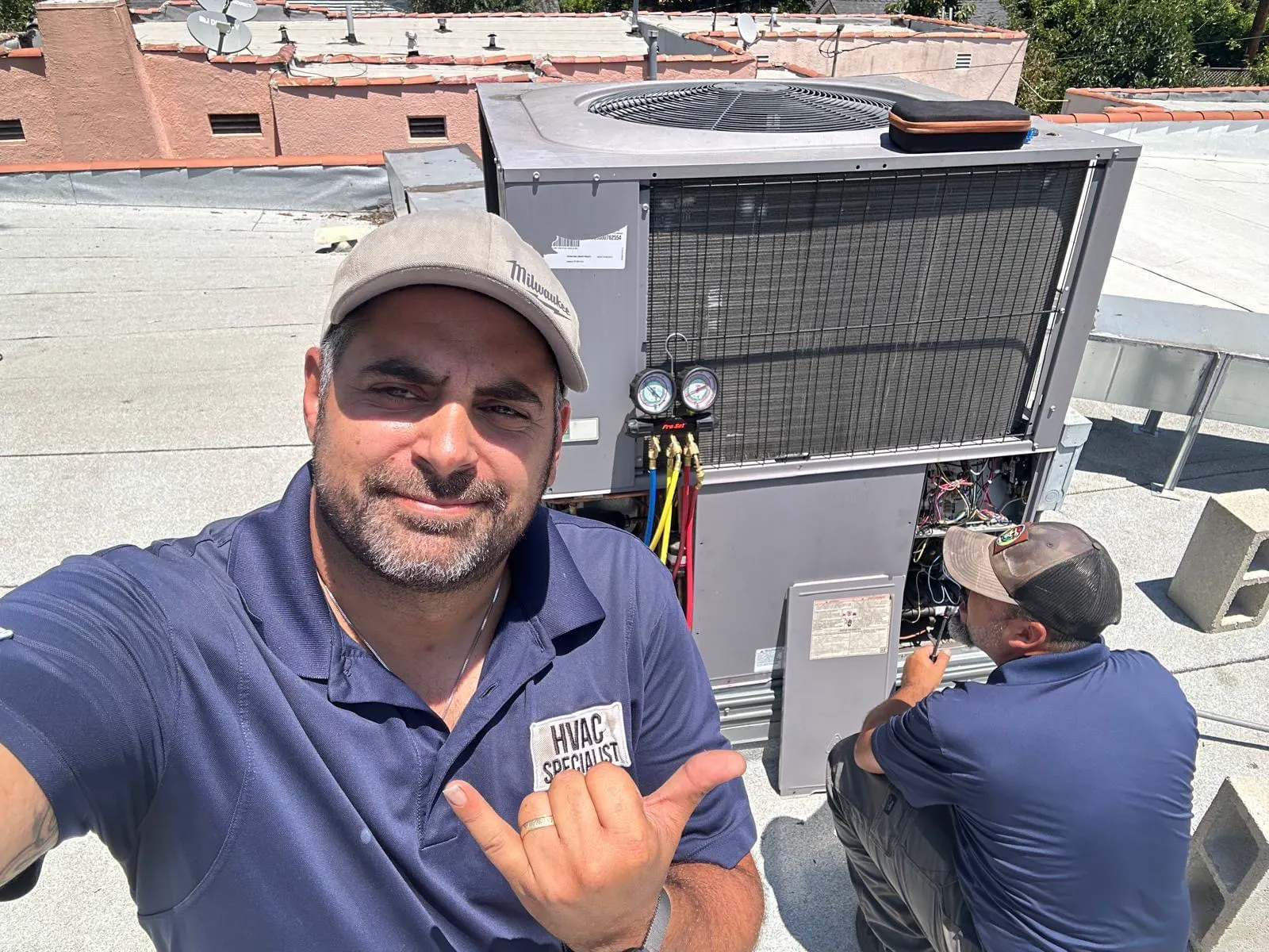 Two Boost technicians servicing a rooftop unit, gauges connected