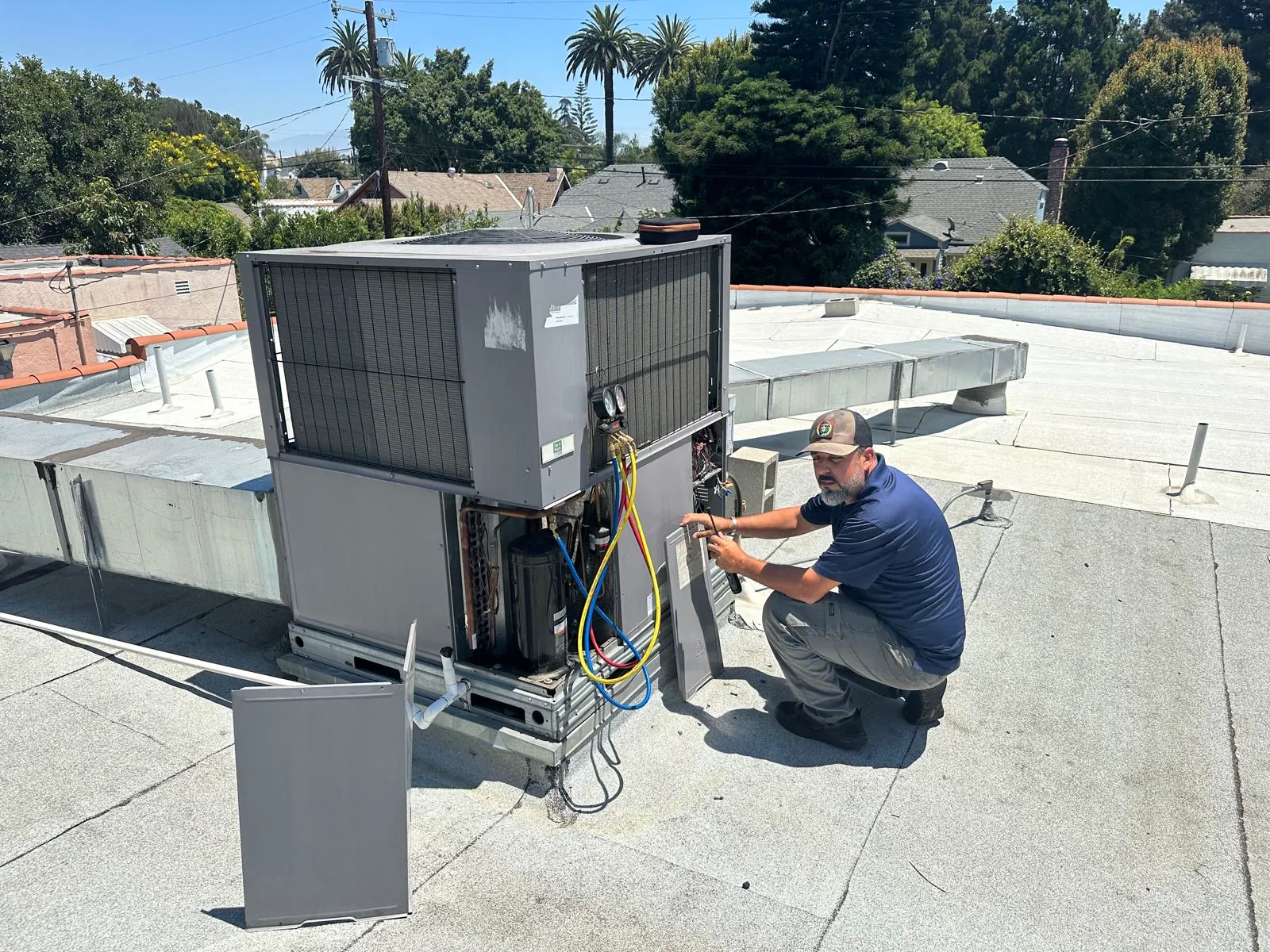 Boost technician at a rooftop package unit above tile roofs and palms