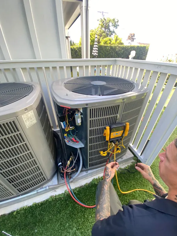 A technician with digital gauges connected to an opened condenser