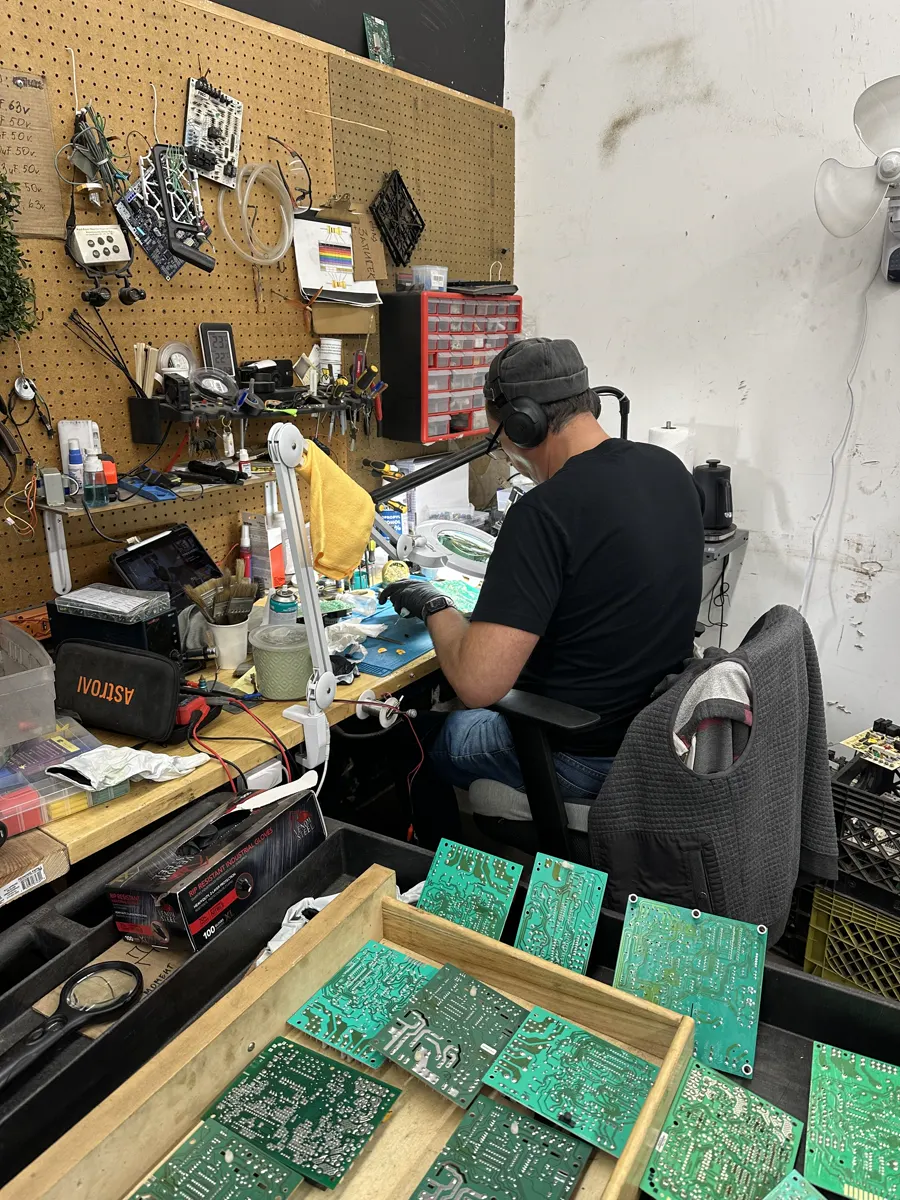 A technician reworking a control board at the bench, with trays of boards in front