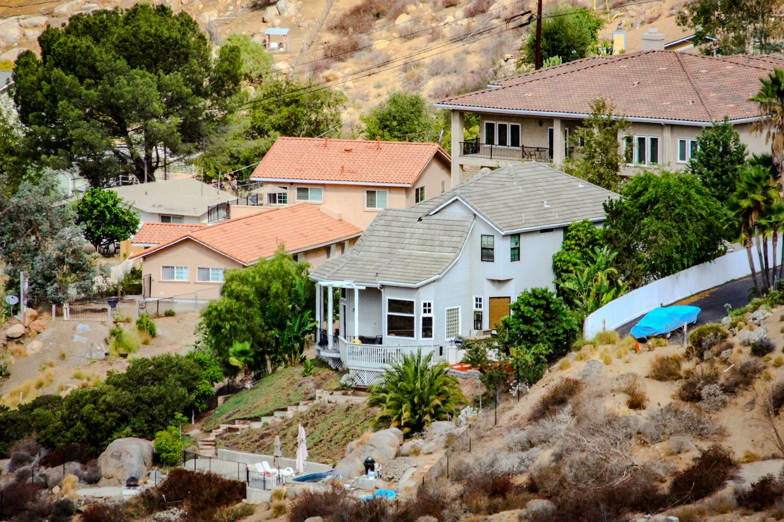 Various houses dot a sunny, arid hillside with scattered trees
