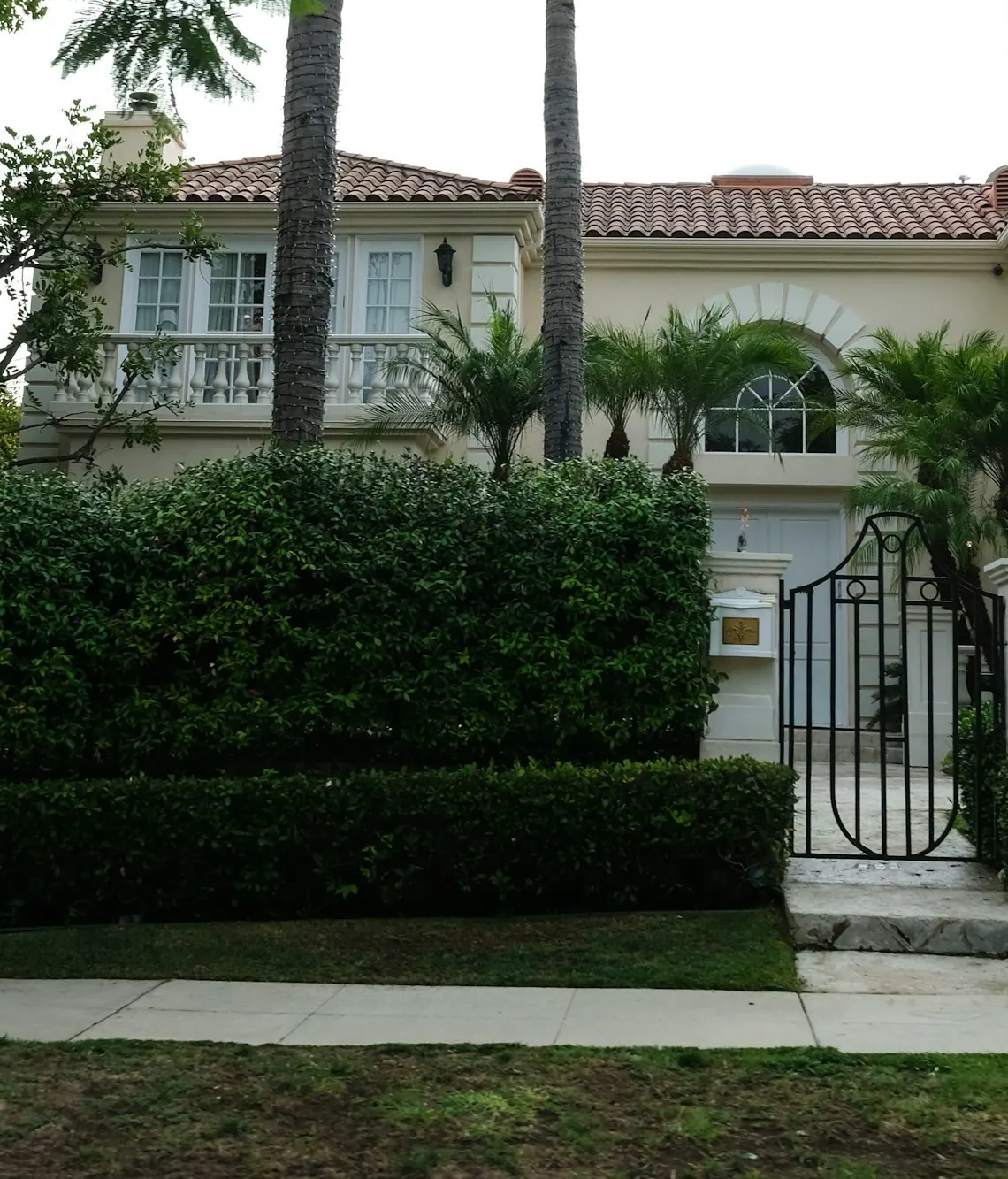 A large, elegant house with manicured hedges and palm trees