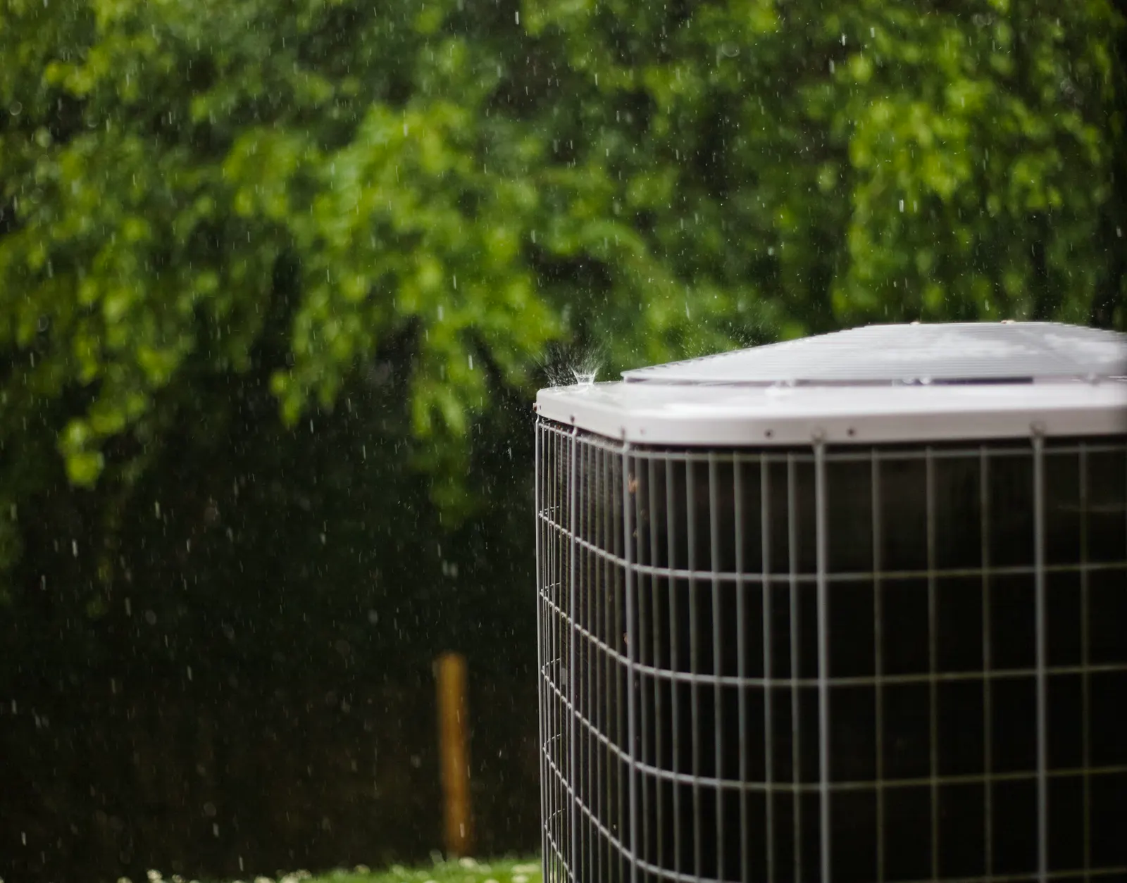 An outdoor heating and cooling unit in the rain beside a garden