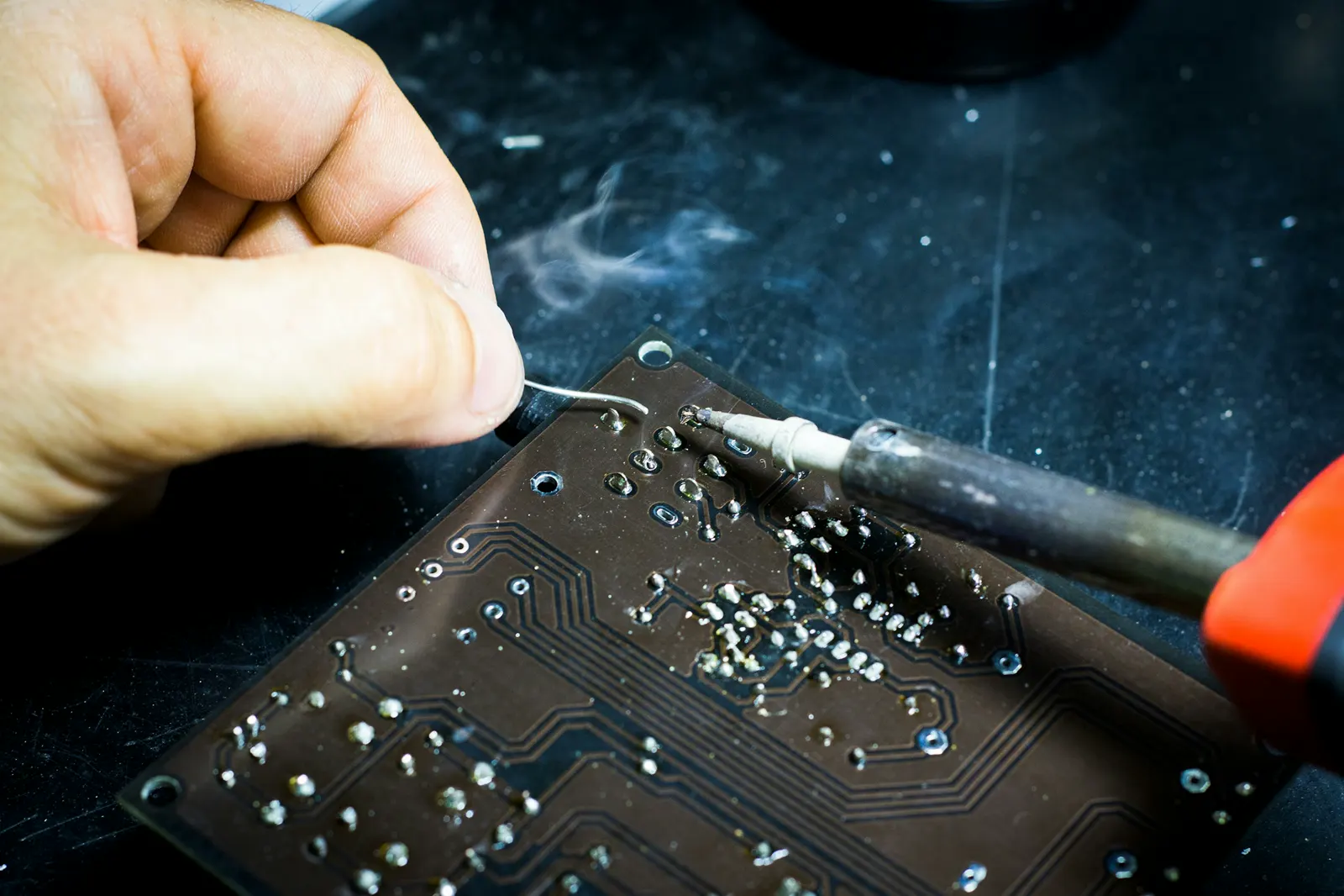 Close-up of hands resoldering joints on a circuit board