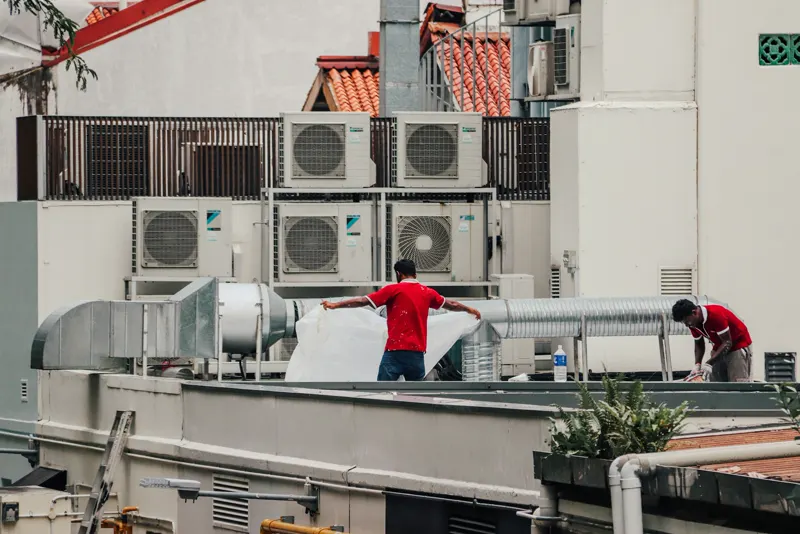 Workers on a rooftop beside air conditioning units and ductwork