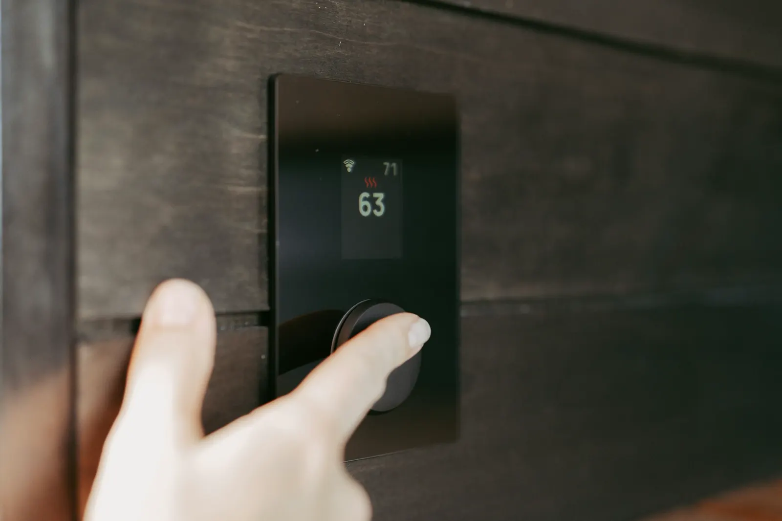 A hand adjusting a wall thermostat
