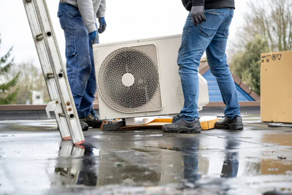 Two installers standing beside a new outdoor condenser on a flat roof