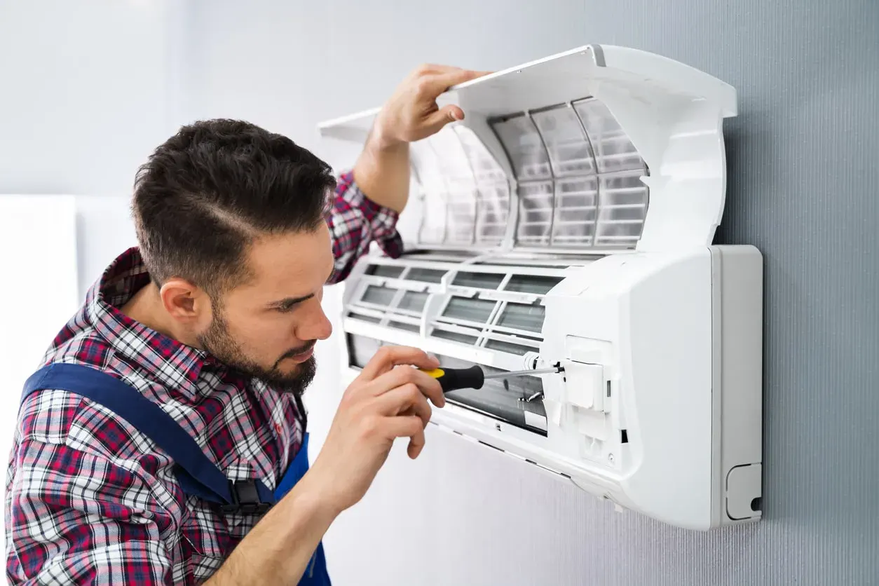 Technician with a screwdriver working inside the cover of a wall-mounted indoor unit