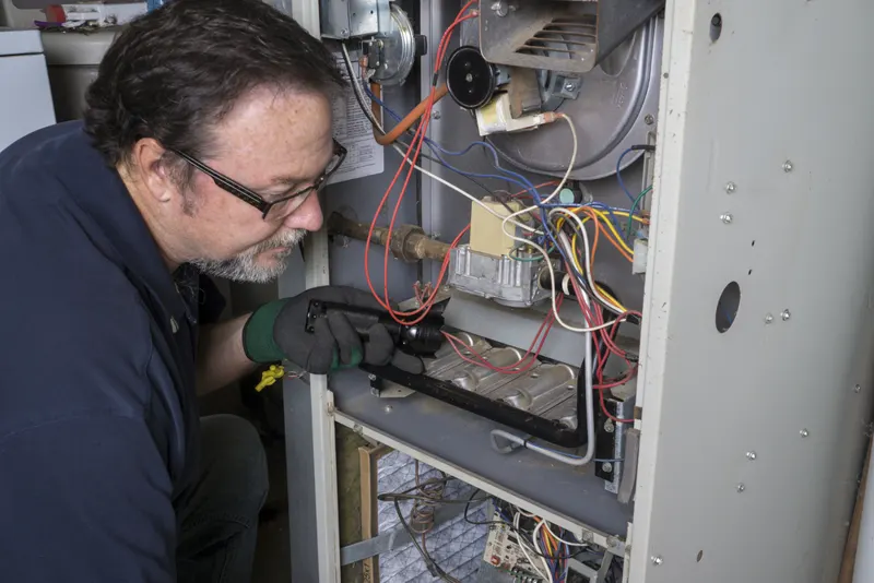 Technician shining a flashlight into the open burner compartment of a gas furnace