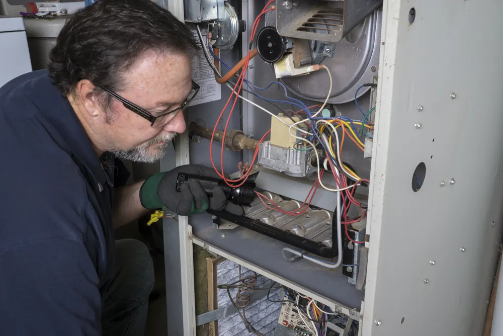 Technician shining a flashlight into the open burner compartment of a gas furnace
